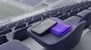 Smartphone auf einem Sitz der Stadiontribüne neben einem schlichten Sportschal